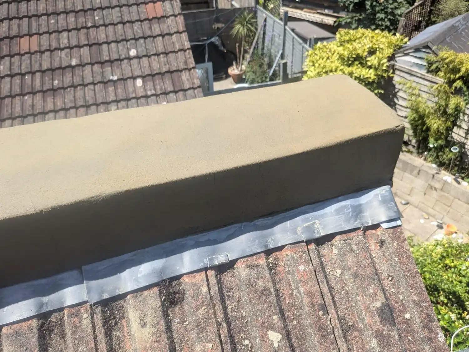 Close-up of roof ridge with mortar rendering and lead flashing on weathered tiles under sunlight.